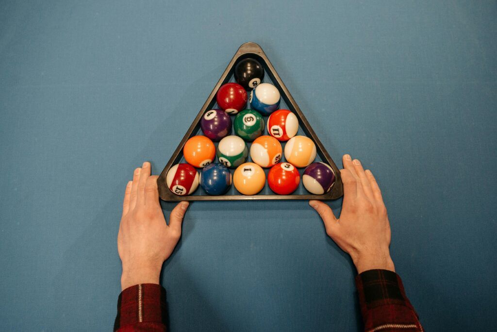 A close-up of hands setting up a colorful billiard ball rack on a pool table.